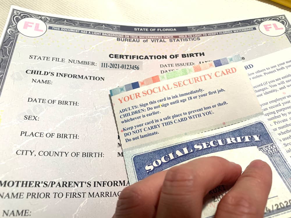 A hand resting on a Social Security card on top of a child's birth certificate indicating adoption records in Texas