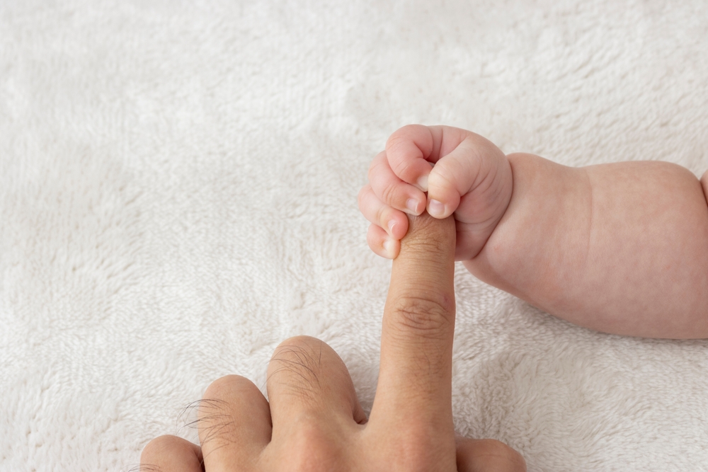 Baby's right hand grasping his father's finger