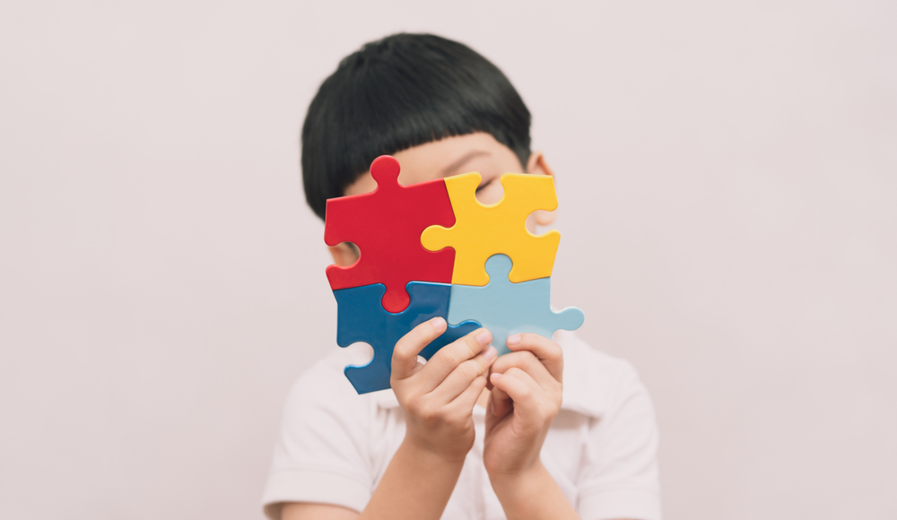 tudio Portrait of young cute Asian kid hold the colorful puzzles pieces, and cover his face. World autism awareness day, Mental health care and Child development concept. Autism Spectrum Disorder.