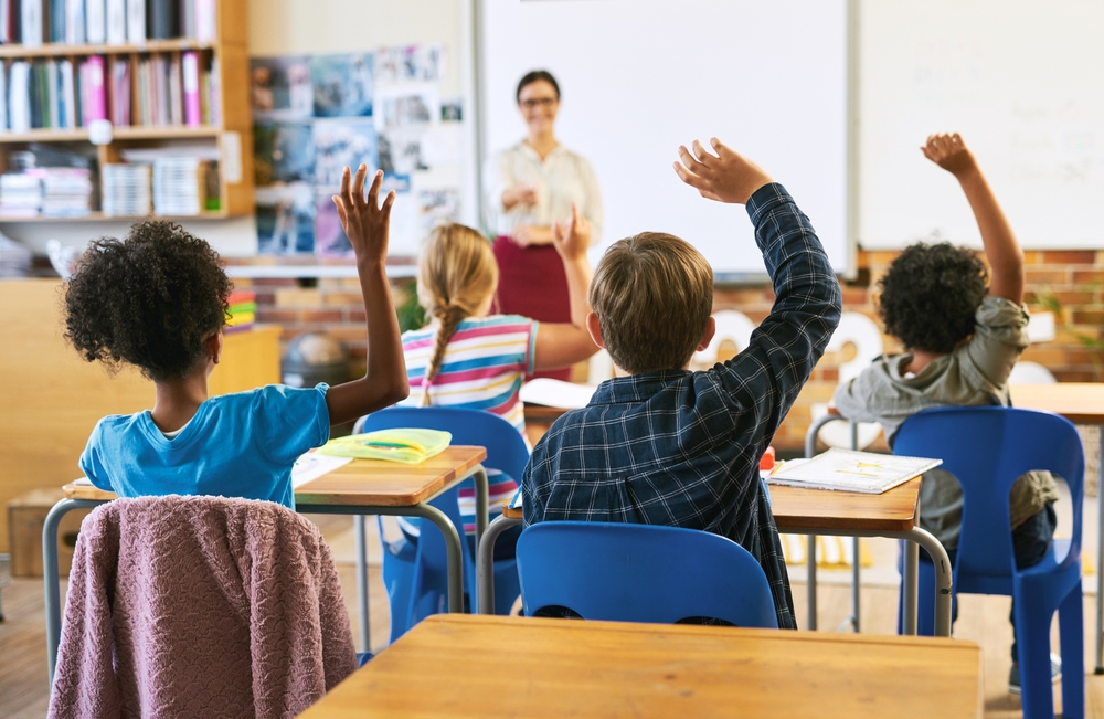 Diverse group of students in a classroom raising their hands, representing transracial parenting resources in use