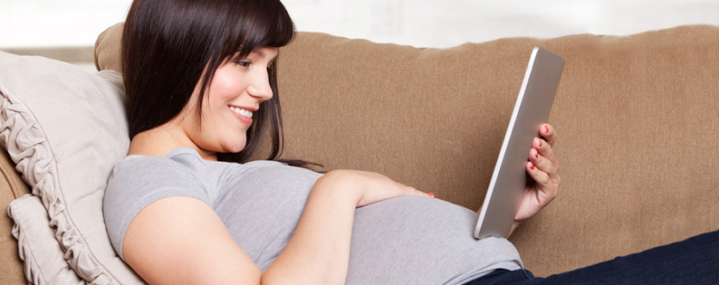 pregnant woman laying on a couch holding a tablet