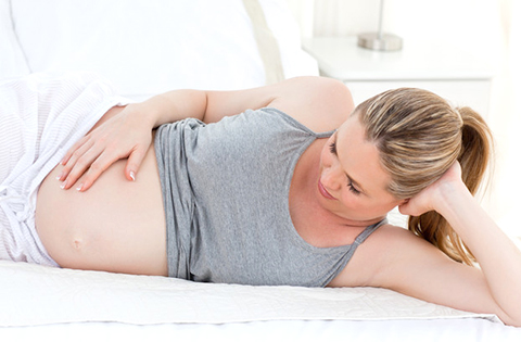 pregnant woman laying on a bed holding her belly