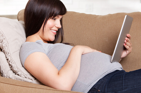 pregnant woman laying on a couch holding a tablet